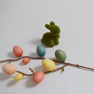 Close-up of a green flocked rabbit figurine next to a branch with colorful spotted Easter eggs
