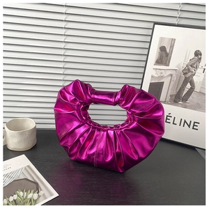 Detailansicht einer metallisch-violetten Rafftasche mit glänzender Faltenstruktur auf Tisch