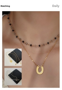 Macro detail of layered U-shaped horseshoe pendant and dark beaded choker necklaces