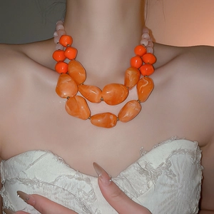 Detail of layered bohemian necklace featuring orange acrylic beads and resin stones