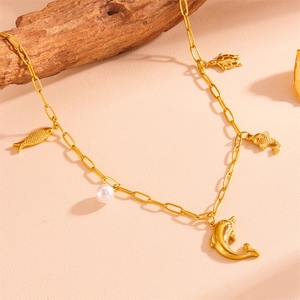 Détail d'un collier chaîne trombone doré avec des breloques marines et une perle blanche