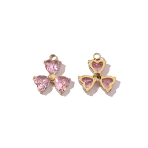 Detailed view of two gold clover pendants with pink heart stones for DIY jewelry