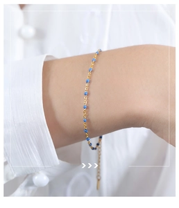 Detail of adjustable gold-plated chain bracelet featuring small blue beads on model's wrist