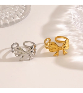 Detailed close-up of 18K gold and silver bow rings on a minimalist textured glass surface