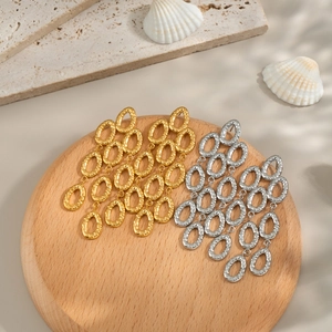 Orecchini a nappa a goccia in oro e argento con trama martellata su vassoio di legno