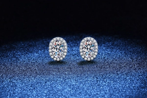 Detail of oval-cut moissanite halo earrings on a textured deep blue background