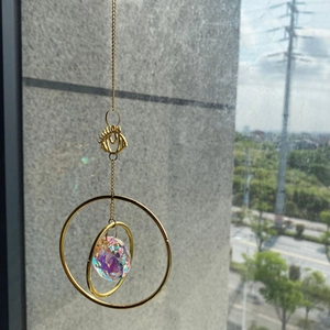 Golden suncatcher with eye metal frame and crystal prism reflecting rainbow light