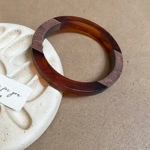Macro view of contrast resin and dark wood拼接 round bangle on a ceramic tray