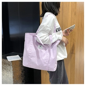 Detail of purple canvas tote bag with wide strap and white woven label on side