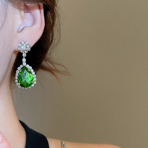 Detailed close-up of a pear-cut emerald green earring with sparkling white diamonds