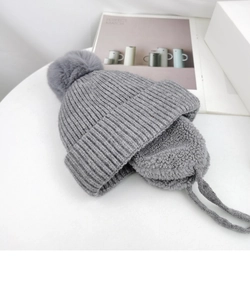 Close-up of grey knitted earflap hat with thick faux sheepskin lining and fluffy pom-pom
