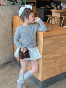 Detailed view of child model wearing a grey ruffle collar top and white pleated skirt