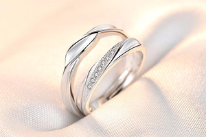 Macro shot of silver couple rings featuring one plain band and one with a small zircon stone