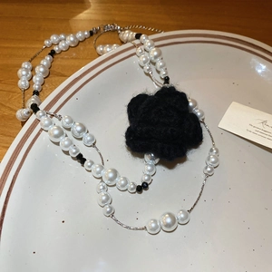 Detail of a double-layer pearl necklace with a black knit camellia flower on a beige plate