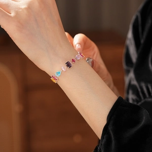 Detail view of a silver bracelet featuring multi-colored gemstones worn on a model's wrist