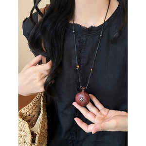 Close-up of a wooden bottle pendant necklace with silver inlay on a black linen dress