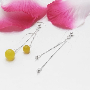 Macro view showing the assembly of silver box chain earrings with yellow ball drops