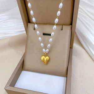 Close-up of a gold heart pendant and white pearl chain displayed in a jewelry box