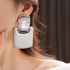 Close-up of oversized silver earrings with rectangular crystals and brushed metal texture