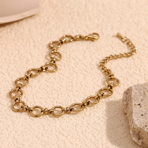 Detail of 14K gold plated stainless steel chain link anklet on textured stone background