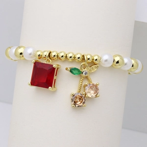 Dettaglio di bracciale con perle dorate e ciondolo a forma di ciliegia con gemme
