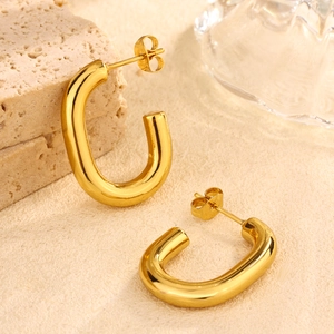 Detail view of golden U-shaped stainless steel earrings on a textured stone background