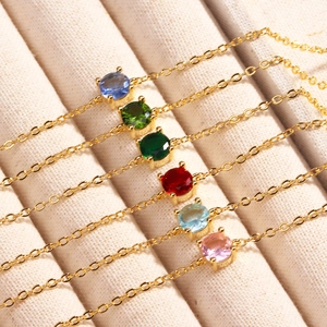 Minimalist gold link bracelet with colorful round zircon stones on a beige tray