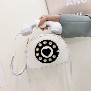 Detail of white vintage telephone-shaped crossbody bag with rotary dial and handset handle