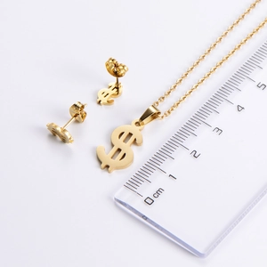 Macro shot of gold dollar sign necklace and earrings with ruler for size reference