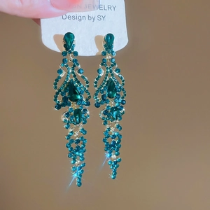 Close-up of emerald green teardrop tassel earrings with golden vintage crystal details