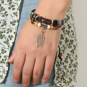Detail of layered brown leather bracelet with wooden beads and silver leaf charm