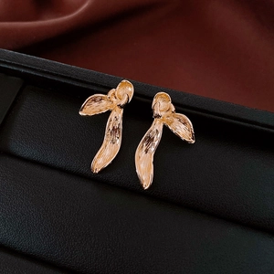 Macro shot of gold floral earrings with textured metal leaves on a black display base