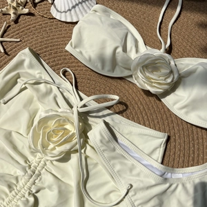 Detailed close-up of cream three-piece bikini set with large 3D fabric rose accents