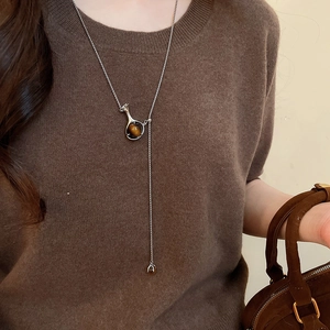 Detail of silver long Y-shaped necklace with brown tiger eye stone on brown sweater