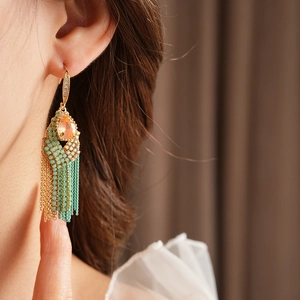 Detail of bohemian gold tassel earring with orange zircon and turquoise beads on model