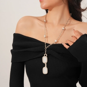 Close-up of a long golden necklace with white oval pendants and zircons on a model