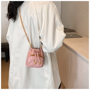 Detailed side view of a pink quilted mini bucket bag with chain strap worn by a model