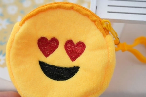 Close-up of a plush yellow round coin purse with red heart eye emoji embroidery and a zipper