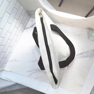 Detail view of canvas tote bag with black zipper closure and textured white fabric