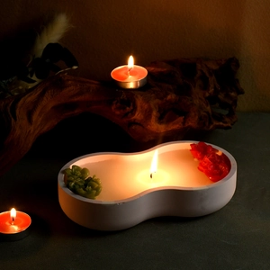 Close-up of a gourd-shaped ceramic candle with floral wax embeds in a dark zen setting