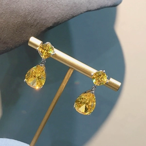 Macro detail of teardrop earrings featuring cushion and pear cut yellow gemstones