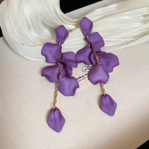 Detail of purple matte rose petal tassel earrings on elegant textured fabric background