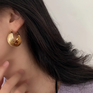 Close-up of golden multi-layer textured hoop earrings on model with vertical stripes