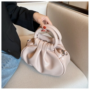 Pink pleated leather cloud bag displayed on a beige sofa in a minimalist home setting
