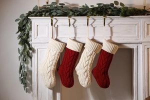 Close-up of four red and beige cable knit Christmas stockings hanging on a white fireplace