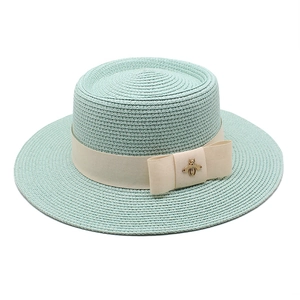 Mint green straw boater hat featuring beige ribbon and gold bee accent in center