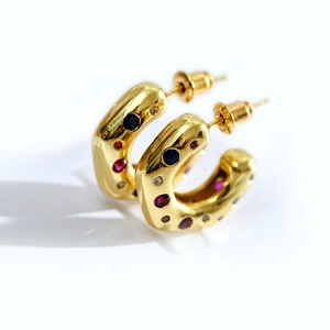 Close-up of chunky gold C-shaped hoop earrings with colorful inlaid crystals and gemstones