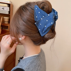 Détail de la pince à cheveux en denim bleu avec motif cœur sur une coiffure élégante