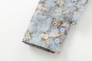 Détail du poignet d'une chemise à fleurs avec deux boutons et texture en coton bleu ciel
