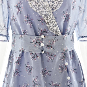 Détail du col en V en dentelle blanche et boutons perles sur robe fleurie bleue